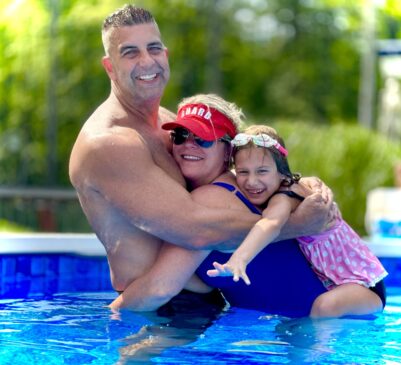 Brett Fraser of Fraser Video enjoying a summer day in the pool with his wife and daughter, all smiling and hugging together.