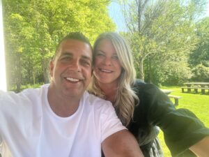Brett Fraser of Fraser Video smiling with his wife outdoors on a sunny day at a picnic area surrounded by trees.